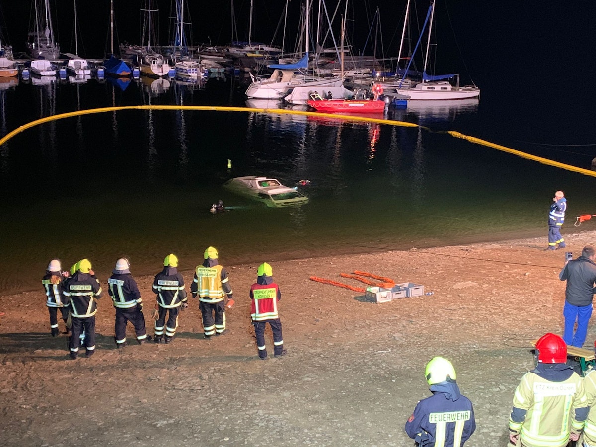 Ein Kleinbus ist im Wasser versunken, mehrere Kräfte der Feuerwehr stehen am Seeufer.