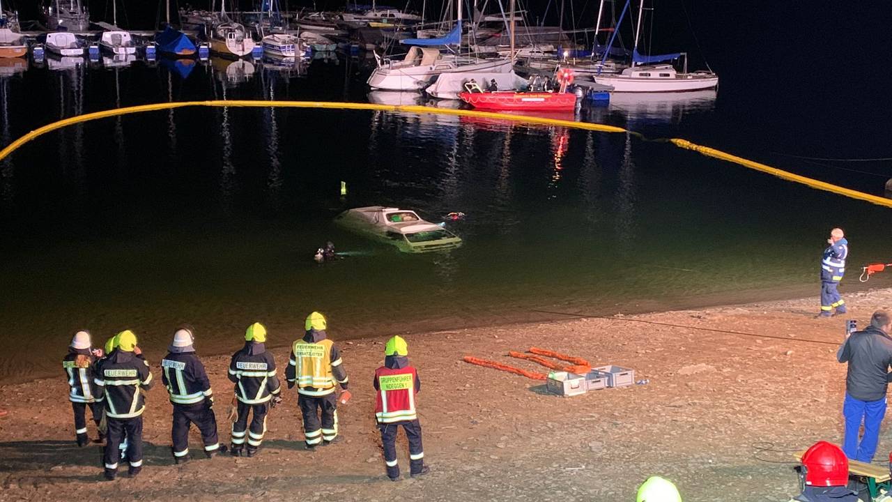 Ein Kleinbus ist im Wasser versunken, mehrere Kräfte der Feuerwehr stehen am Seeufer.