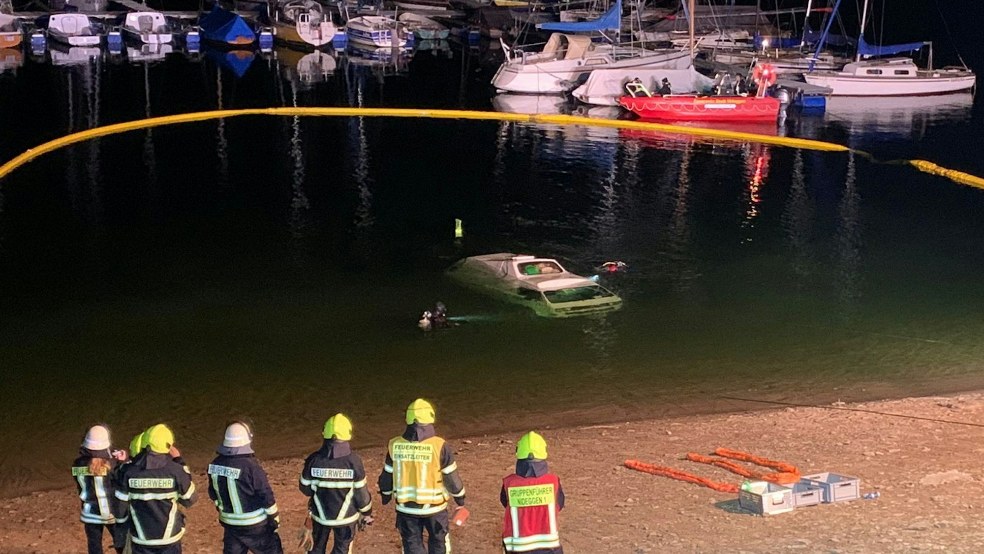Ein Kleinbus ist im Wasser versunken, mehrere Kräfte der Feuerwehr stehen am Seeufer.