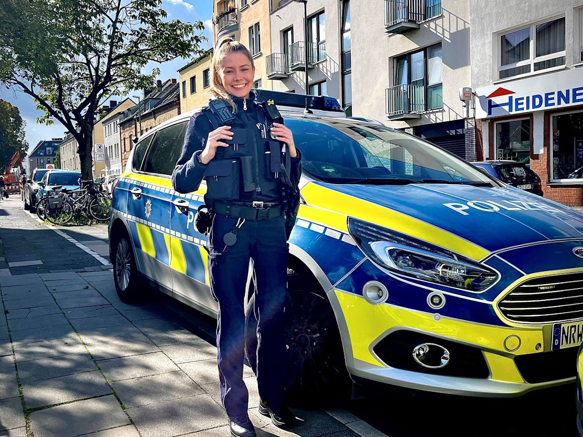 Polizeikommissarin Mira Asbach (29) von der Kölner Polizei steht vor einem Streifenwagen.