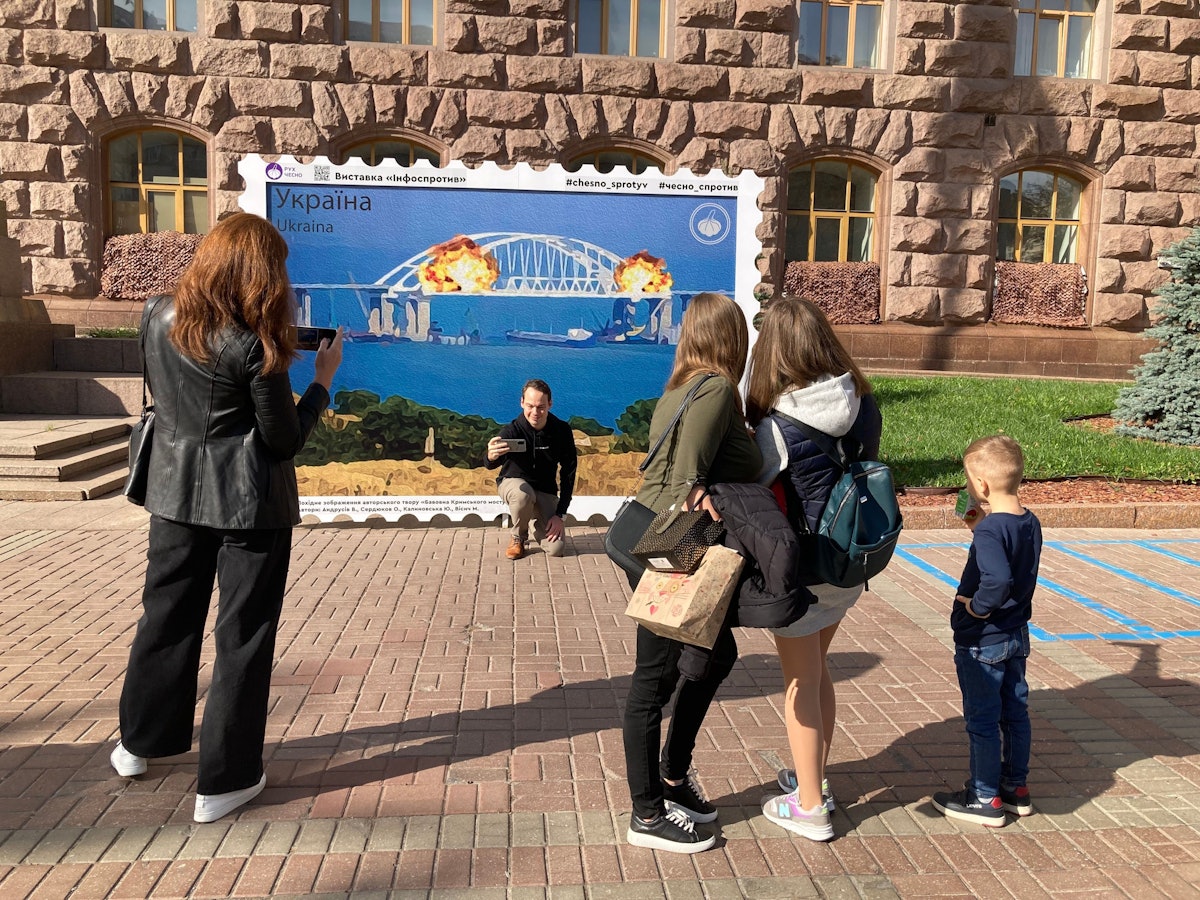 Menschen fotografieren sich am 9. Oktober 2022 in Kyjiw vor einem Plakat, das Explosionen auf der für Russland wichtigen Krym-Brücke zeigt.