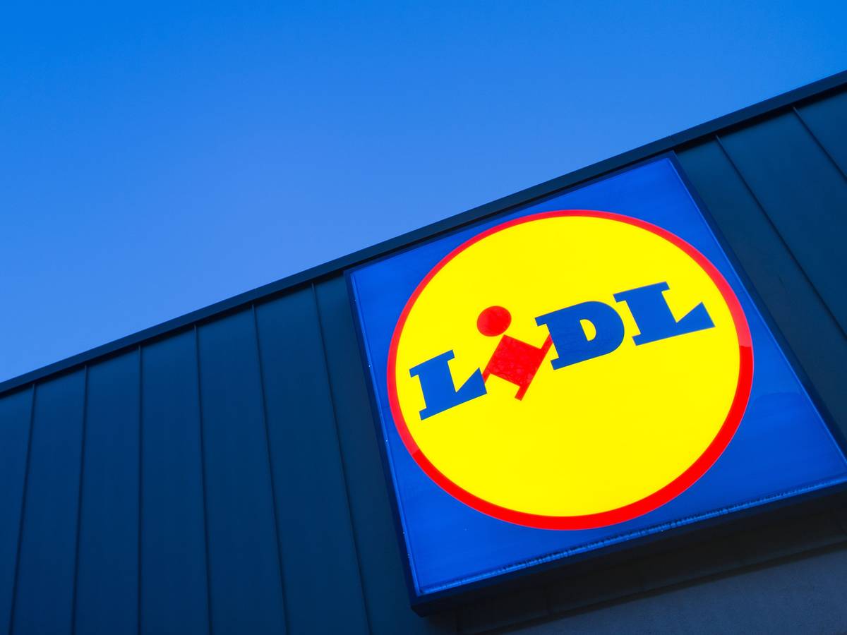Das Logo eines Lidl-Supermarktes in Berlin-Reinickendorf leuchtet vor dem Abendhimmel.