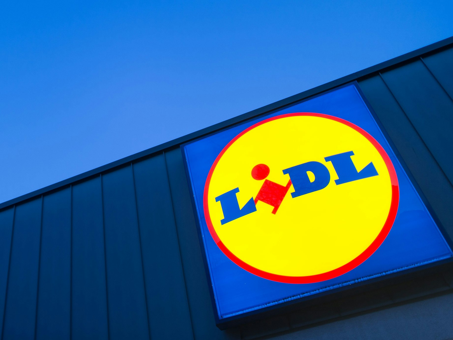 Das Logo eines Lidl-Supermarktes in Berlin-Reinickendorf leuchtet vor dem Abendhimmel.