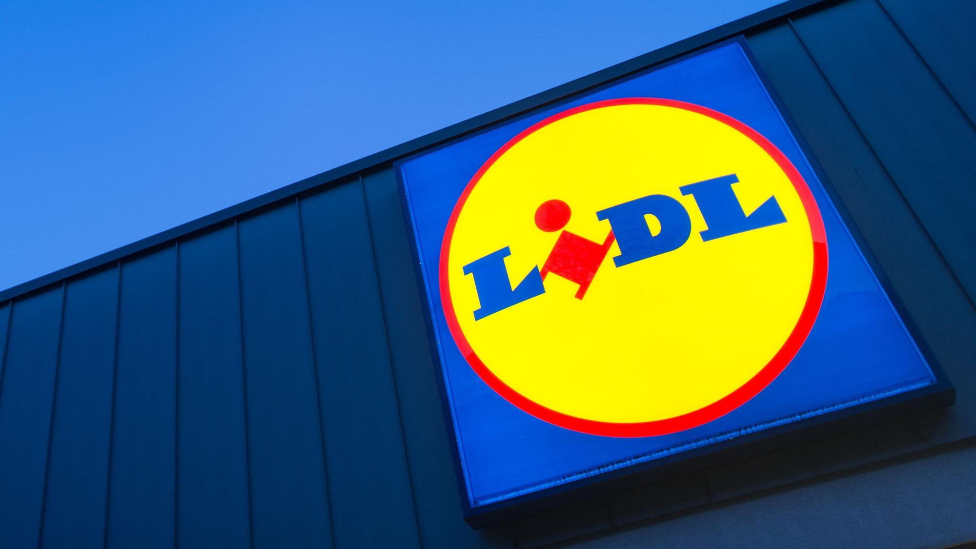 Das Logo eines Lidl-Supermarktes in Berlin-Reinickendorf leuchtet vor dem Abendhimmel.