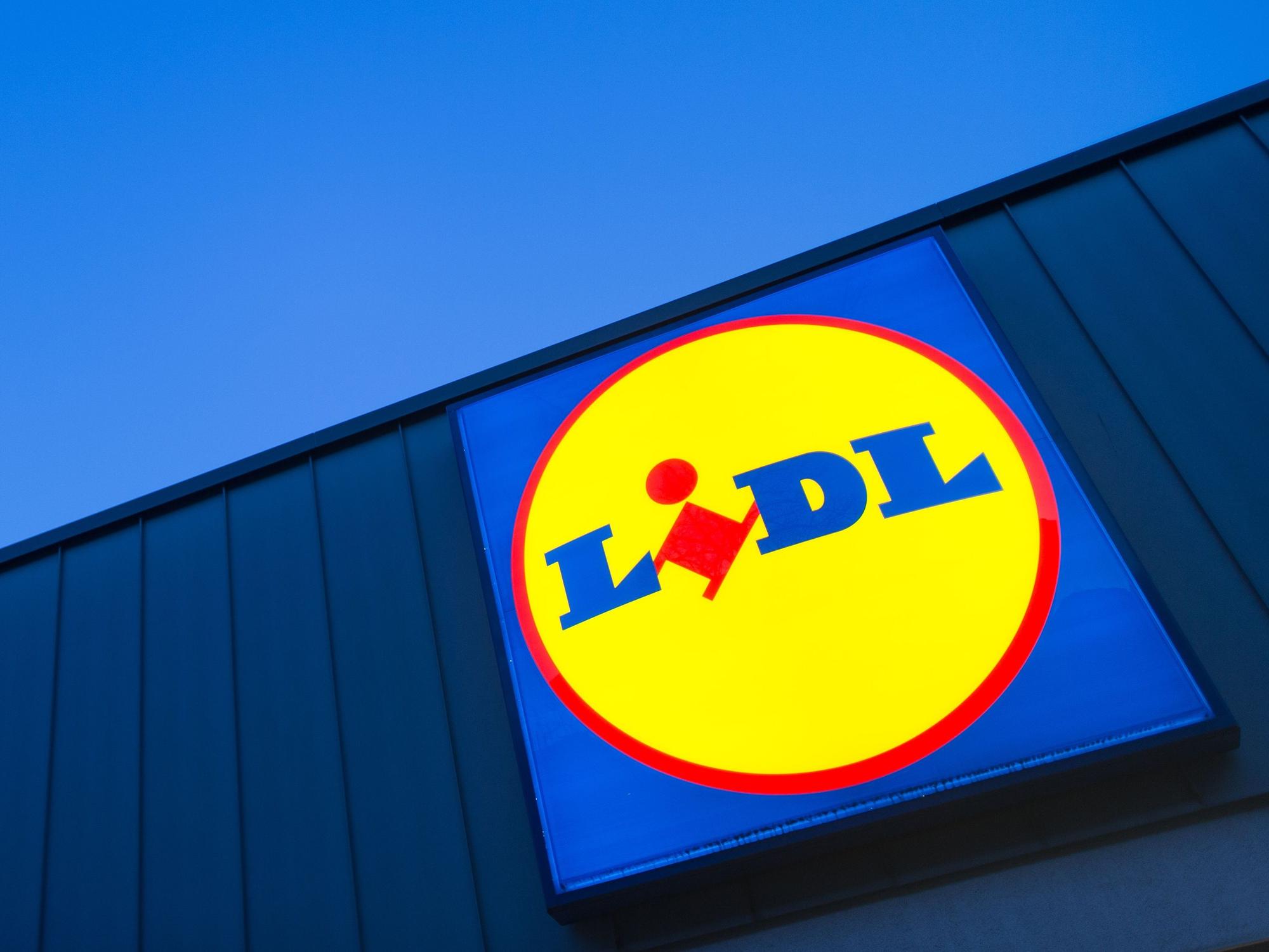 Das Logo eines Lidl-Supermarktes in Berlin-Reinickendorf leuchtet vor dem Abendhimmel.