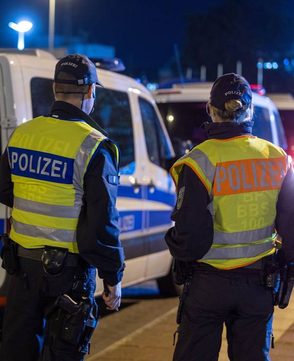 Mehrere Polizeifahrzeuge stehen an der Straße, davor eine Polizistin mit einem Kollege.
