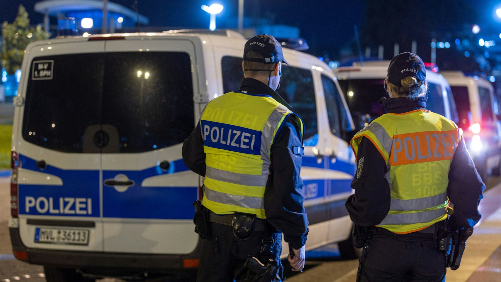 Mehrere Polizeifahrzeuge stehen an der Straße, davor eine Polizistin mit einem Kollege.