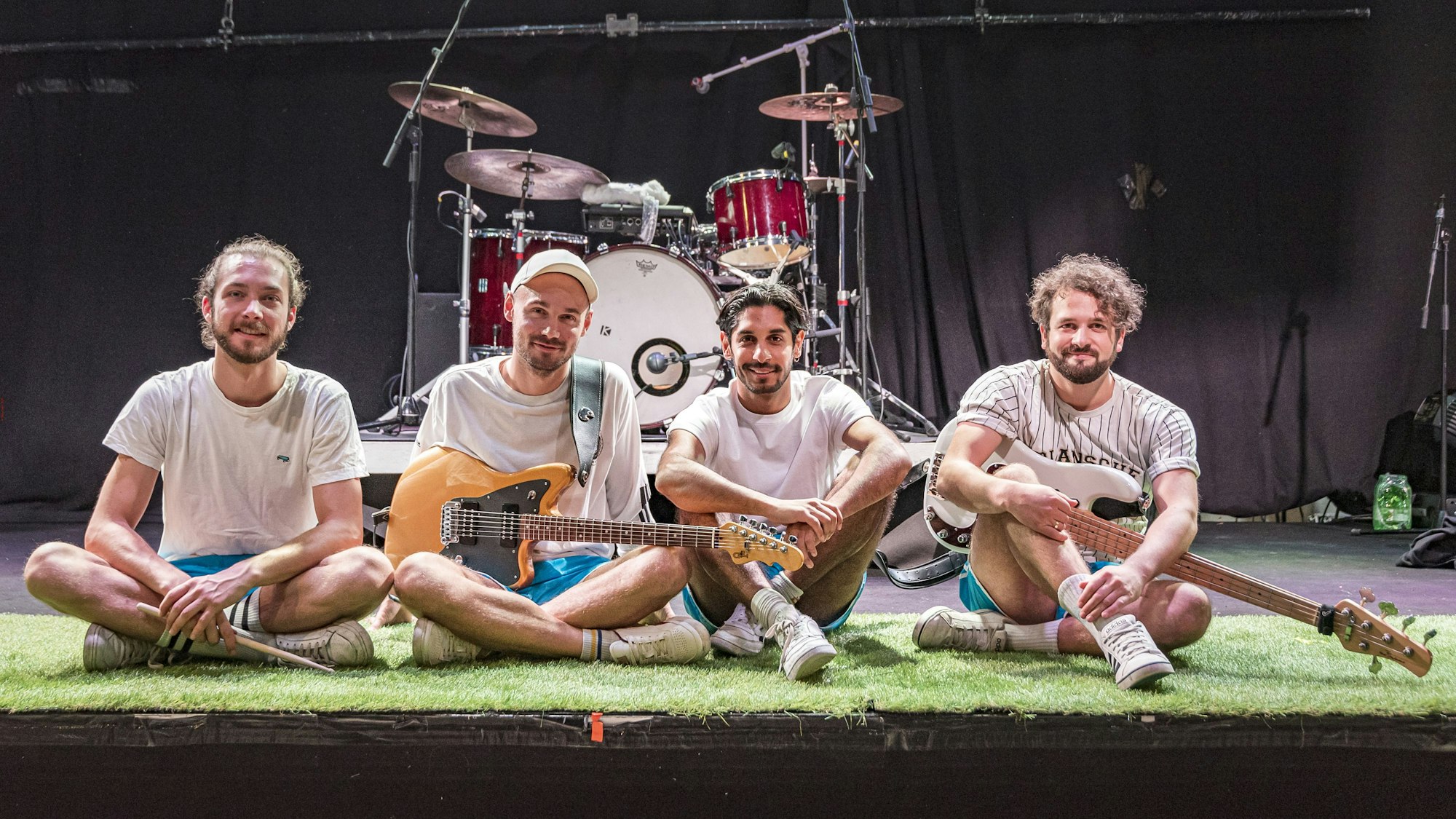 Die vier Mitglieder von Planschemalöör sitzen auf der Bühne und schauen in die Kamera.