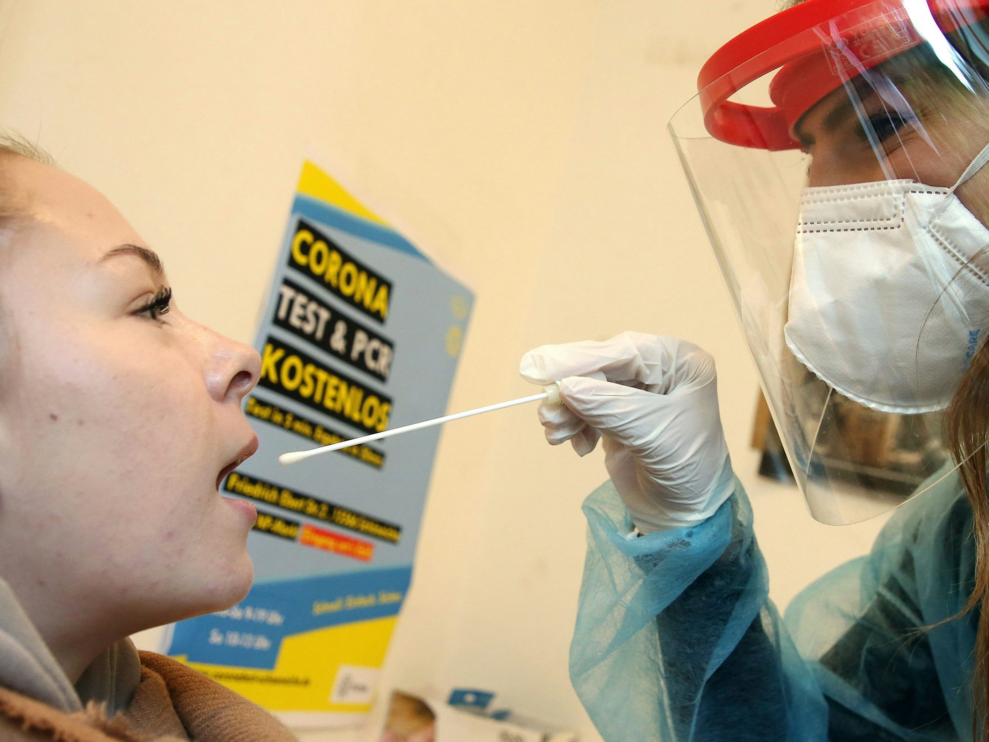 Eine junge Frau lässt von einer Mitarbeiterin einer Corona-Teststelle mit einem Teststäbchen einen Abstrich machen, um sich auf Corona zu testen.