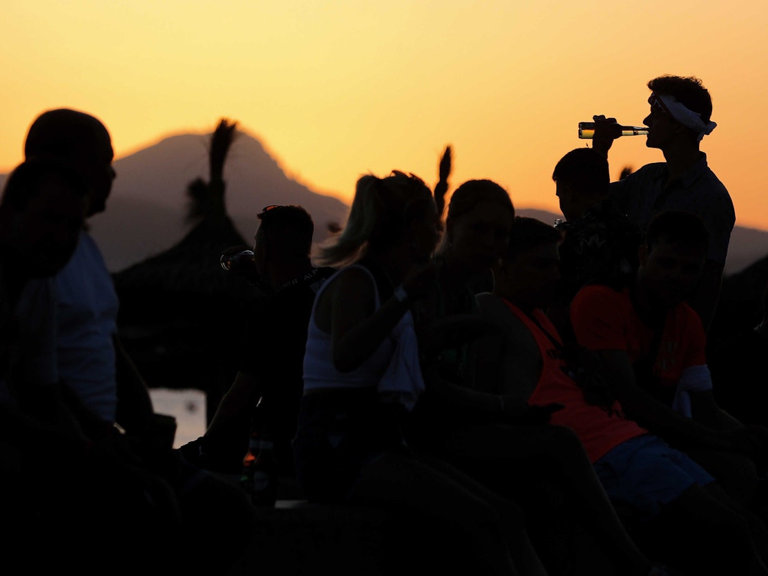 Das undatierte Symbolfoto zeigt mehrere Menschen, die vor einem Sonnenuntergang feiern.