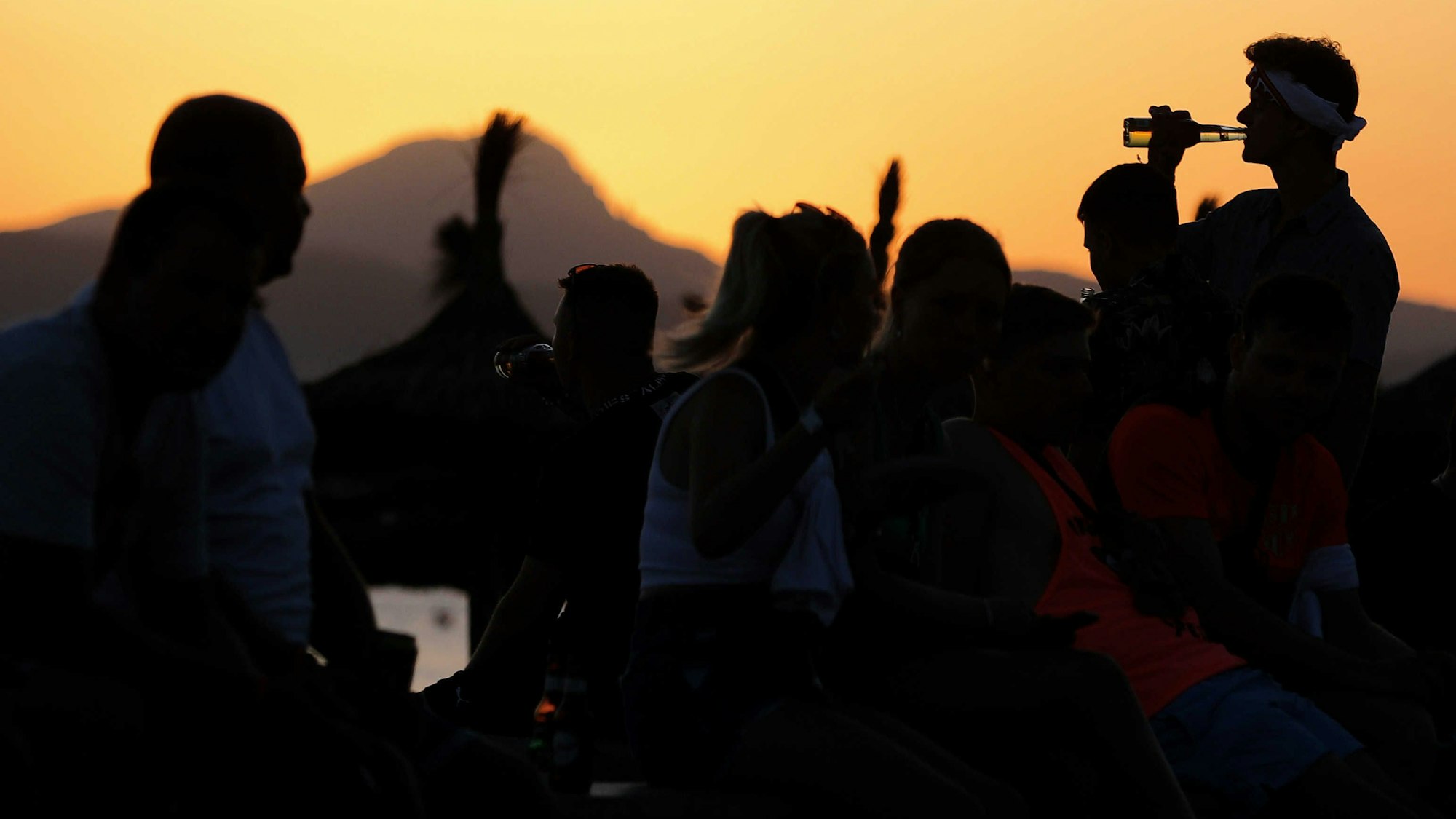 Das undatierte Symbolfoto zeigt mehrere Menschen, die vor einem Sonnenuntergang feiern.
