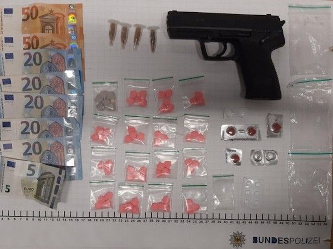 Bargeld, Tüten mit Drogen und eine Pistole liegen auf einem weißen Tisch.