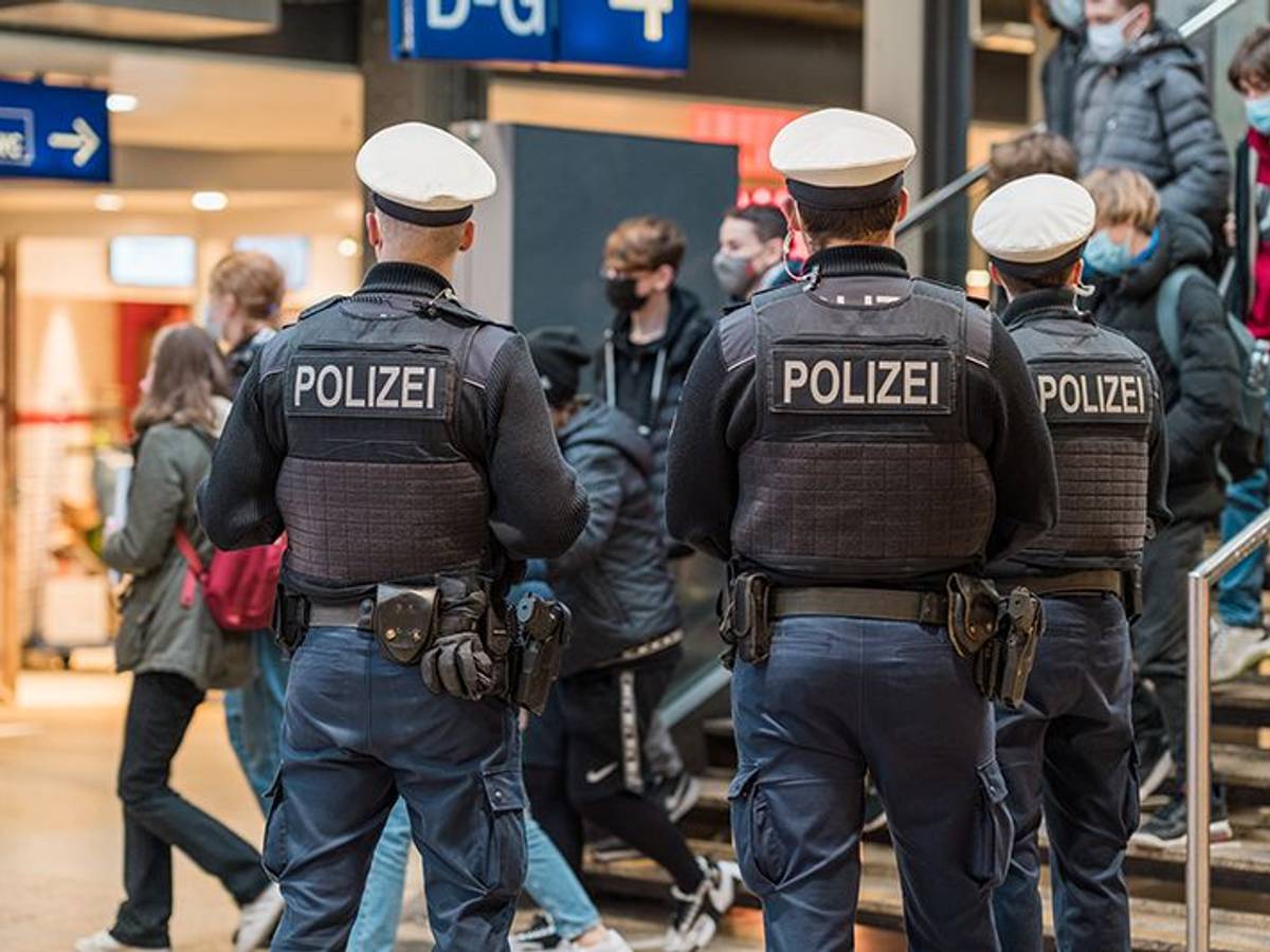 Drei Bundespolizisten stehen im Kölner Hauptbahnhof und beobachten Reisende, die eine Treppe herunterkommen.