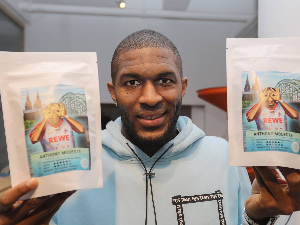 Anthony Modeste hält zwei Tüten des Kaffees in der Hand, auf dem er selbst in Jubelpose zu sehen ist.