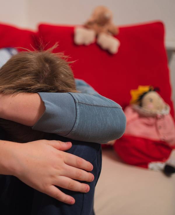 Ein Junge kauert sich auf seinem Bett zusammen.