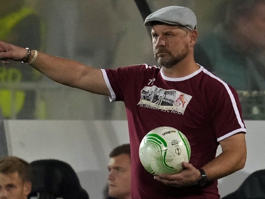Steffen Baumgart hält bei einem Spiel des 1. FC Köln in der Conference League den Ball in der Hand und gibt mit ausgestrecktem Zeigefinger Anweisungen