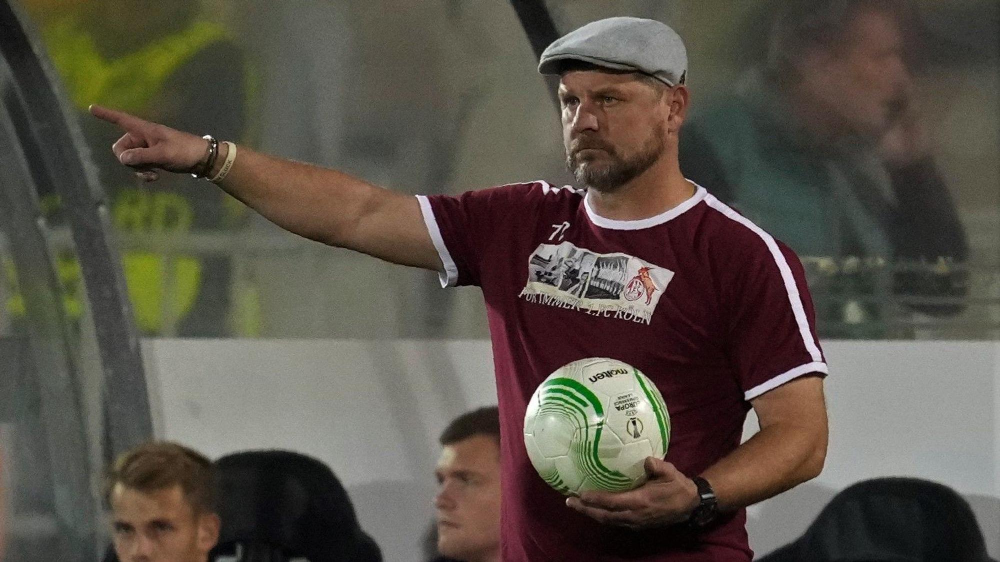 Steffen Baumgart hält bei einem Spiel des 1. FC Köln in der Conference League den Ball in der Hand und gibt mit ausgestrecktem Zeigefinger Anweisungen