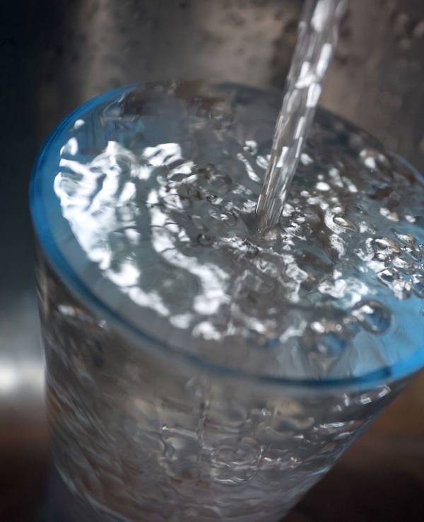 Leitungswasser fließt in ein Glas, das in einem Spülbecken steht.