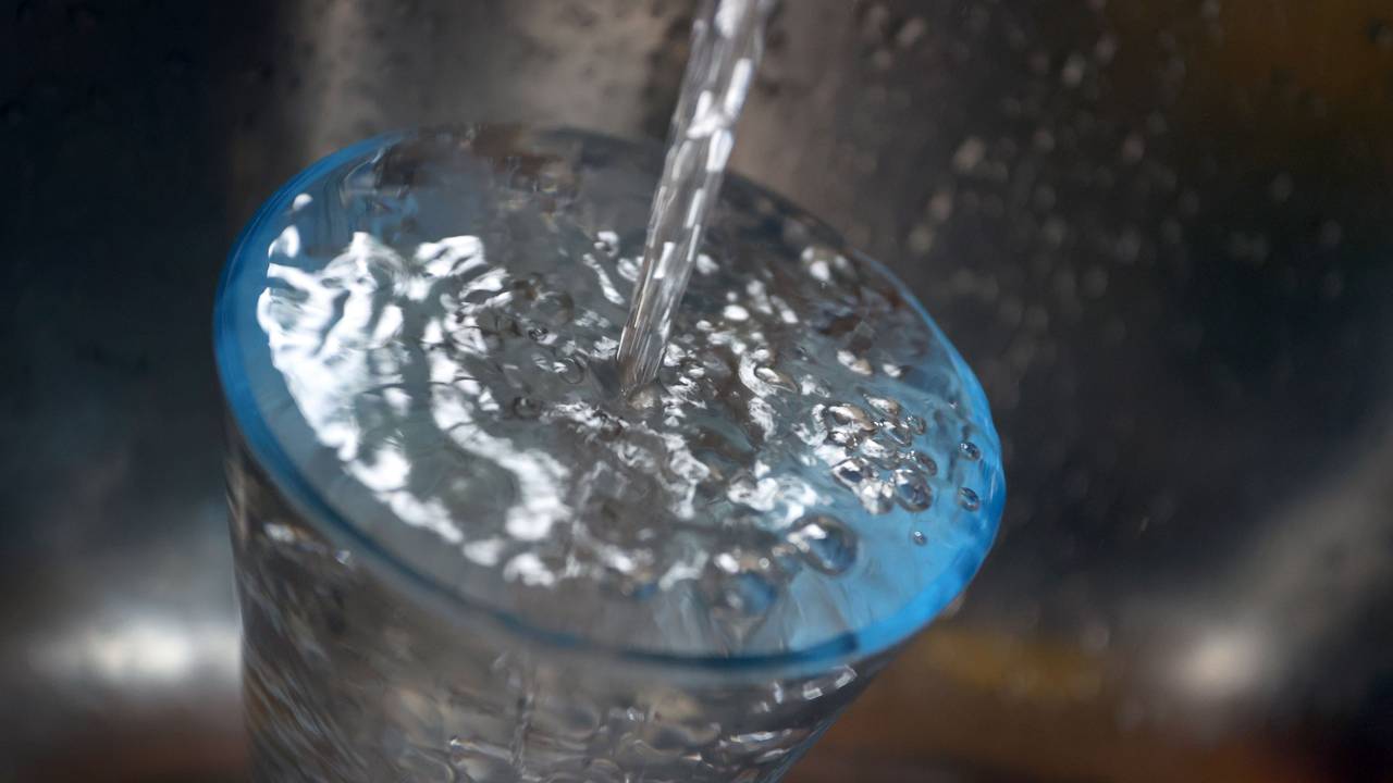 Leitungswasser fließt in ein Glas, das in einem Spülbecken steht.