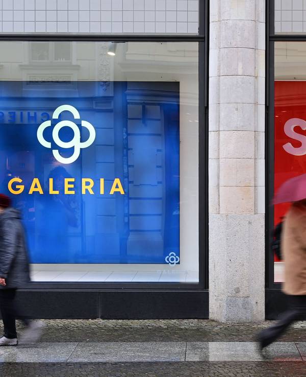 Das undatierte Symbolfoto zeigt zwei Menschen, die an einem Schaufenster mit großen Plakaten vorbeigehen.