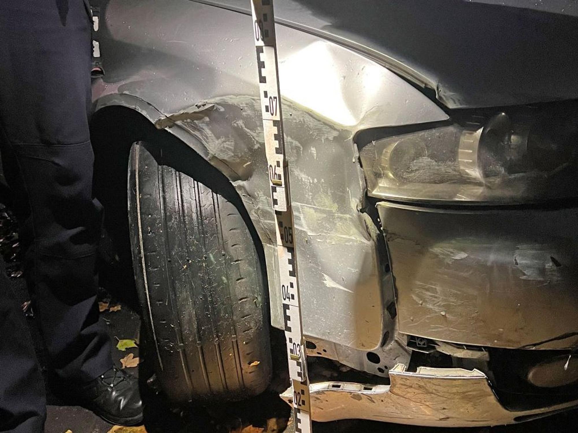 Ein Polizist hält einen Maßstab an die beschädigte Stelle des Autos..