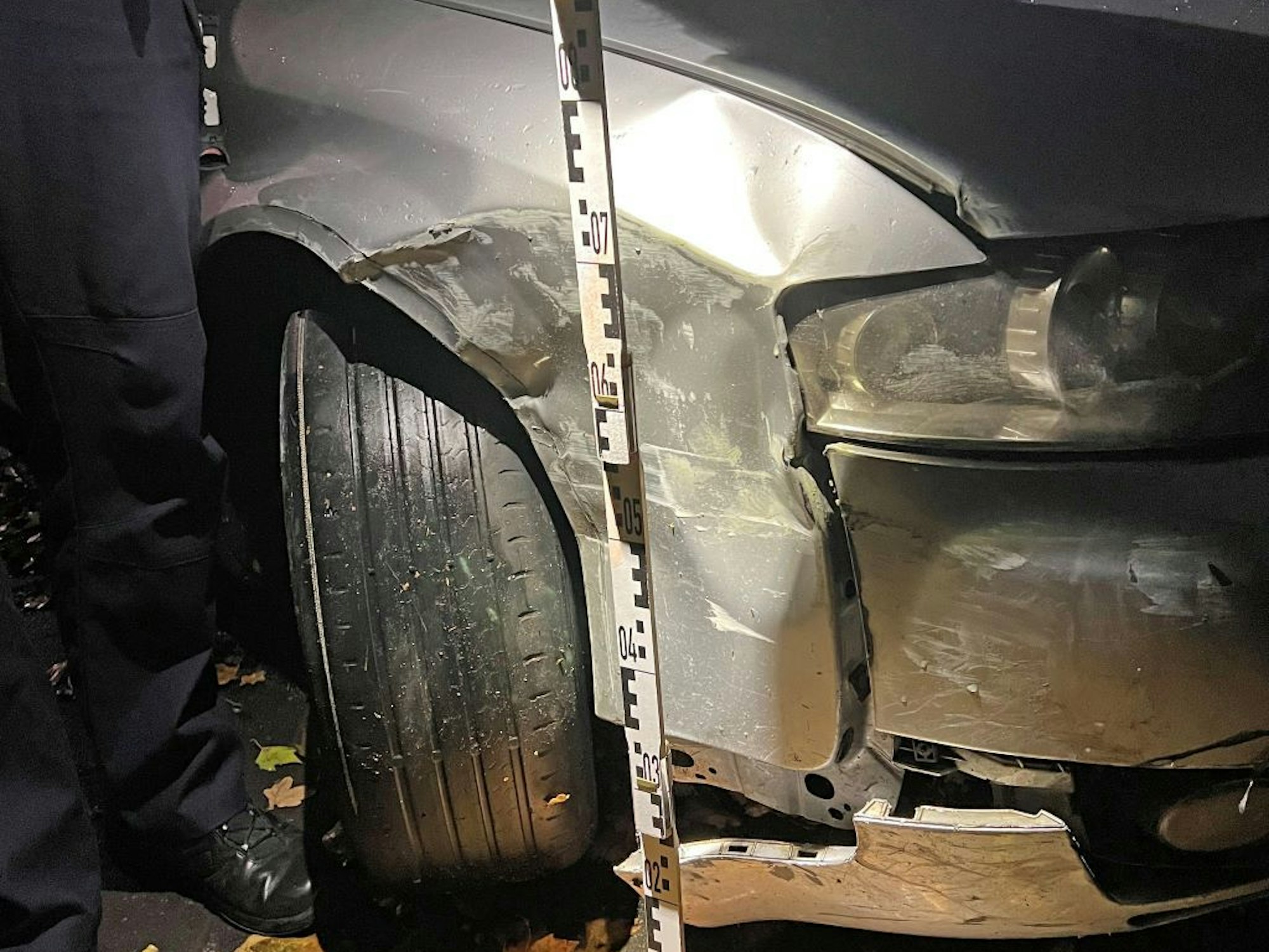 Ein Polizist hält einen Maßstab an die beschädigte Stelle des Autos..