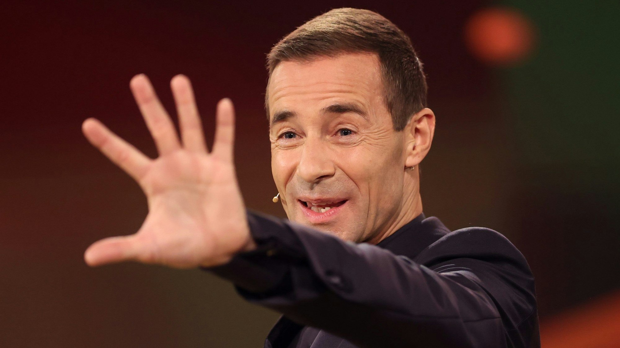 Kai Pflaume steht auf der Bühne und winkt mit der linken Hand.