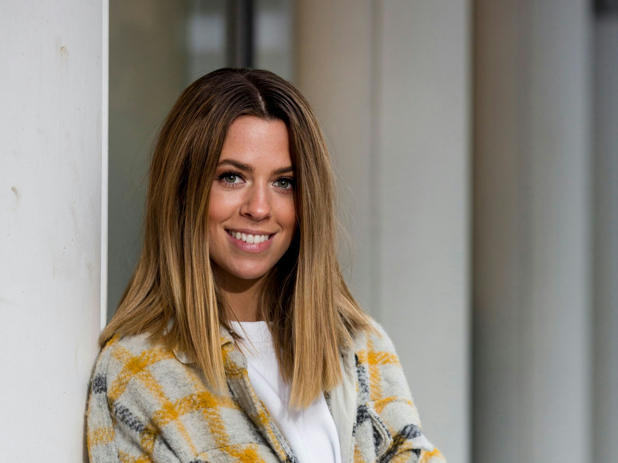 Vanessa Mai lacht fröhlich in einer bunten Strickjacke in die Kamera.