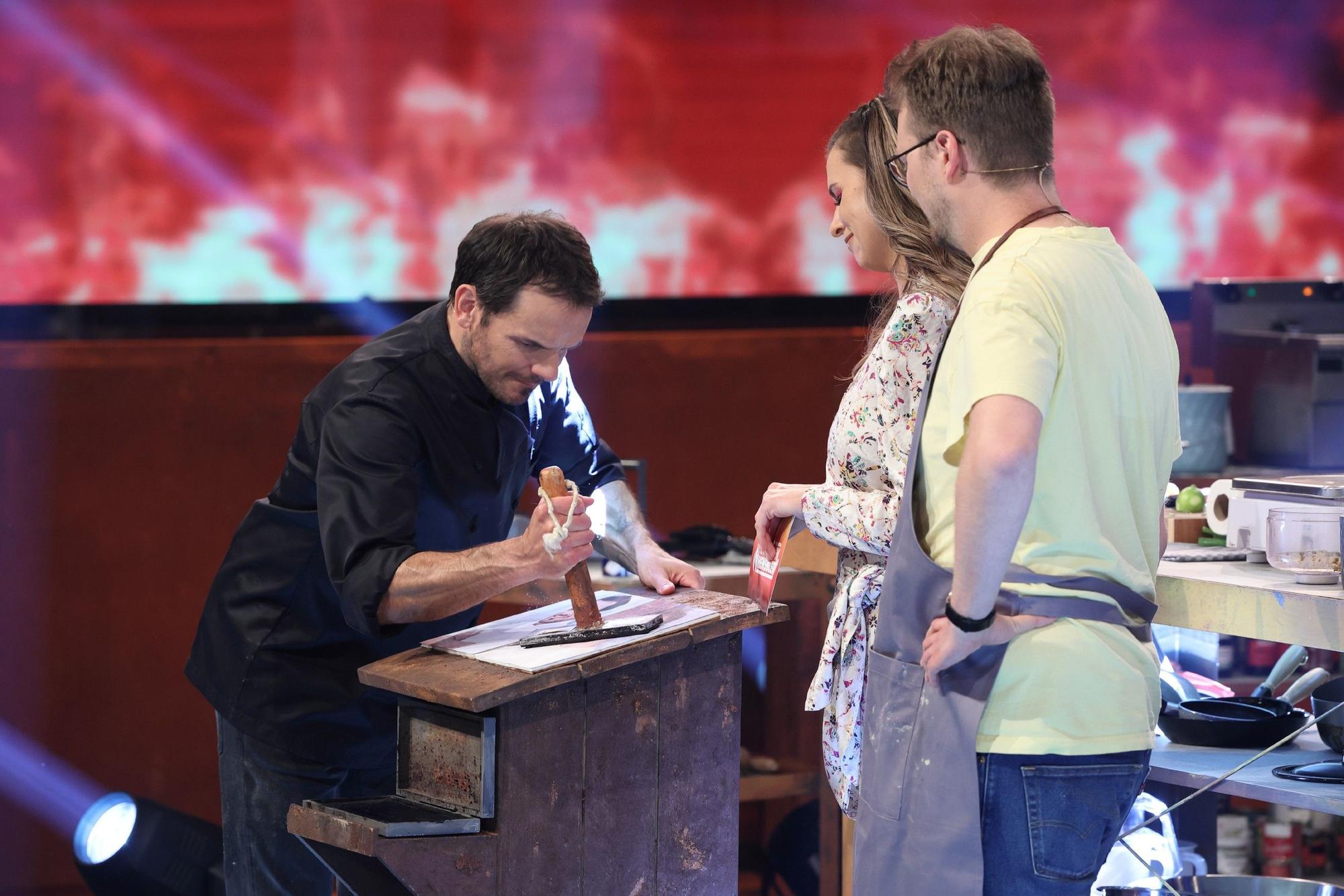 Steffen Henssler demonstriert Laura Wontorra und Maxi Gstettenbauer, wie er etwas an einem Tisch zerstampft.