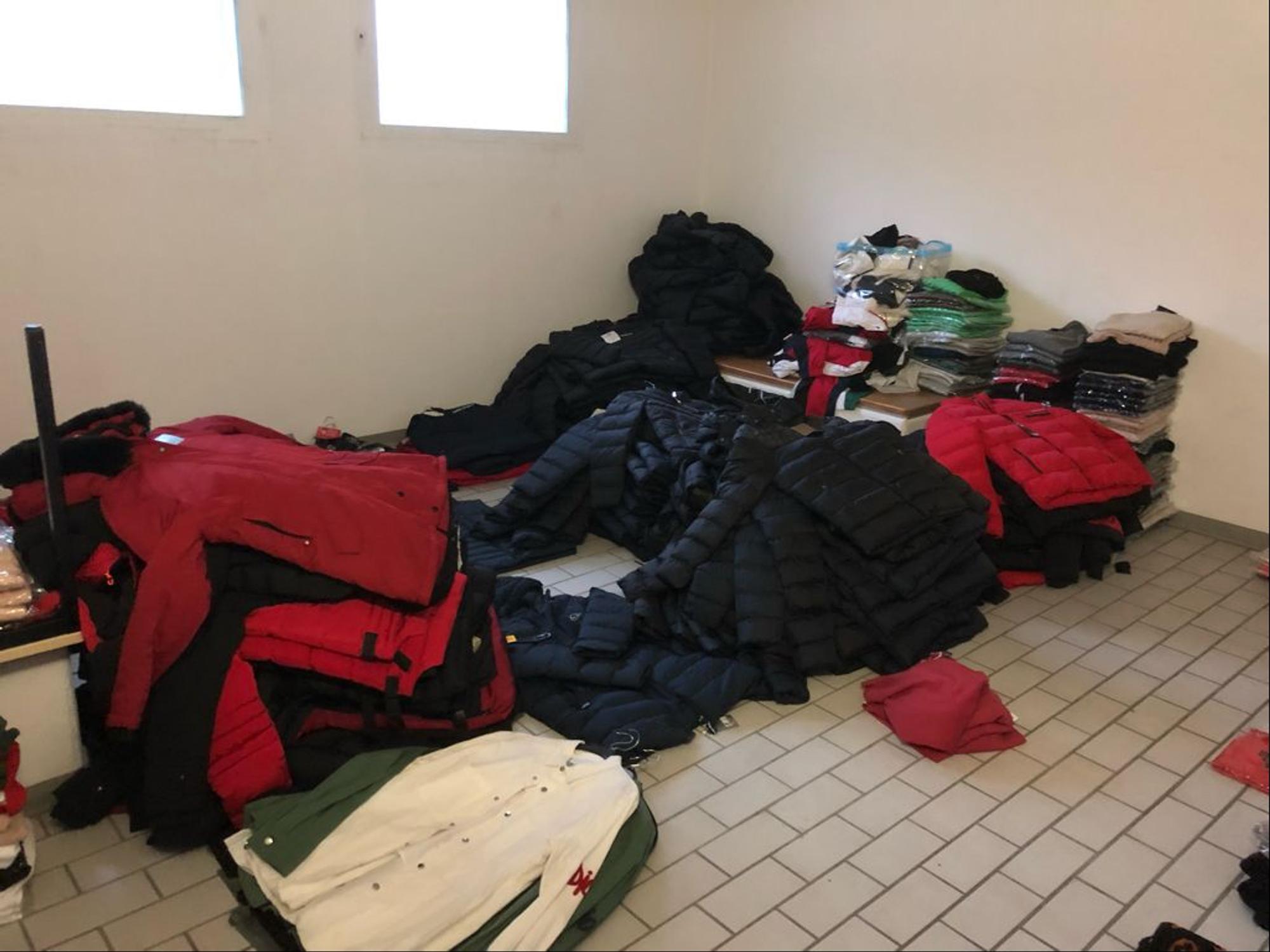 Ein Stapel mit Klamotten liegt in einem Abstellraum. Die Klamotten sind gefälscht und wurden sichergestellt.