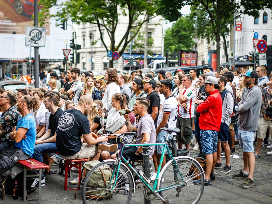 Fußballfans stehen während der Fußball-EM an einer Kneipe und verfolgen gemeinsam ein Spiel.