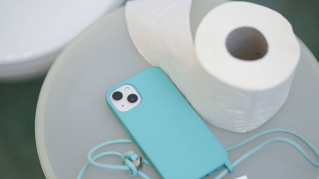 Ein Smartphone und eine Klopapierrolle liegen neben einer Toilette auf einem Badeimer.