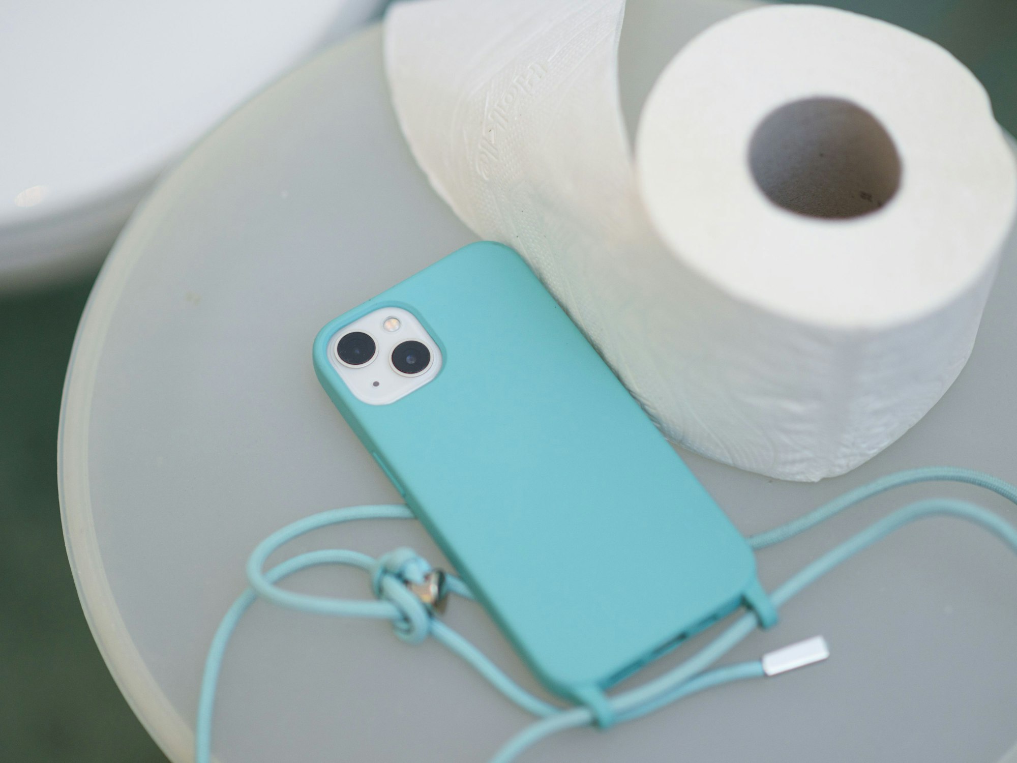 Ein Smartphone und eine Klopapierrolle liegen neben einer Toilette auf einem Badeimer.