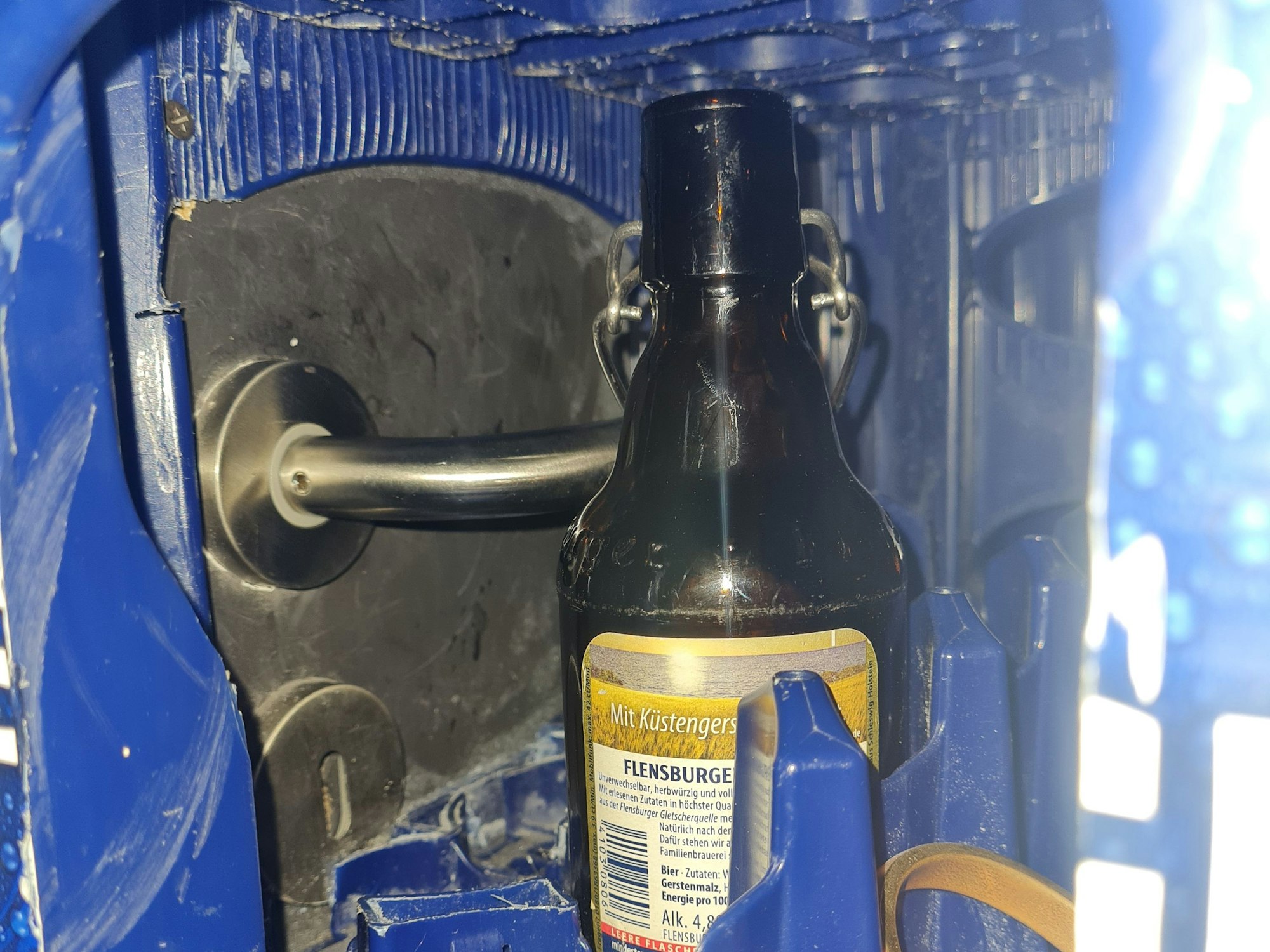 Ein Türgriff ist durch die Öffnung eines Bierkastens zu sehen.