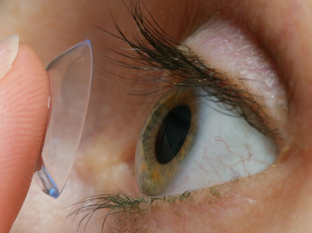 Eine Frau setzt sich eine Kontaktlinse auf das Auge.
