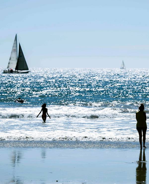 Das undatierte Symbolfoto zeigt einen Strand und das dahinterliegende Meer mit mehreren Menschen und zwei Segelbooten.