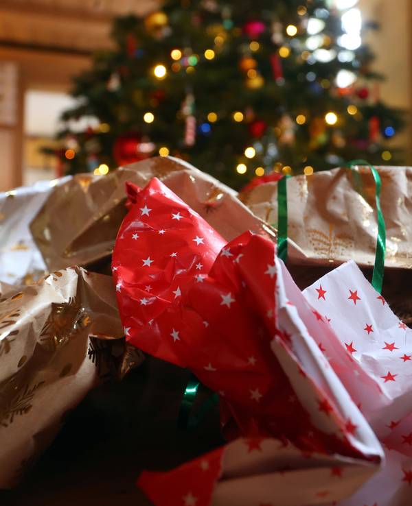 Geschenkpapier von ausgepackten Weihnachtsgeschenken liegt auf dem Boden eines Zimmers vor einem geschmücktem Weihnachtsbaum.