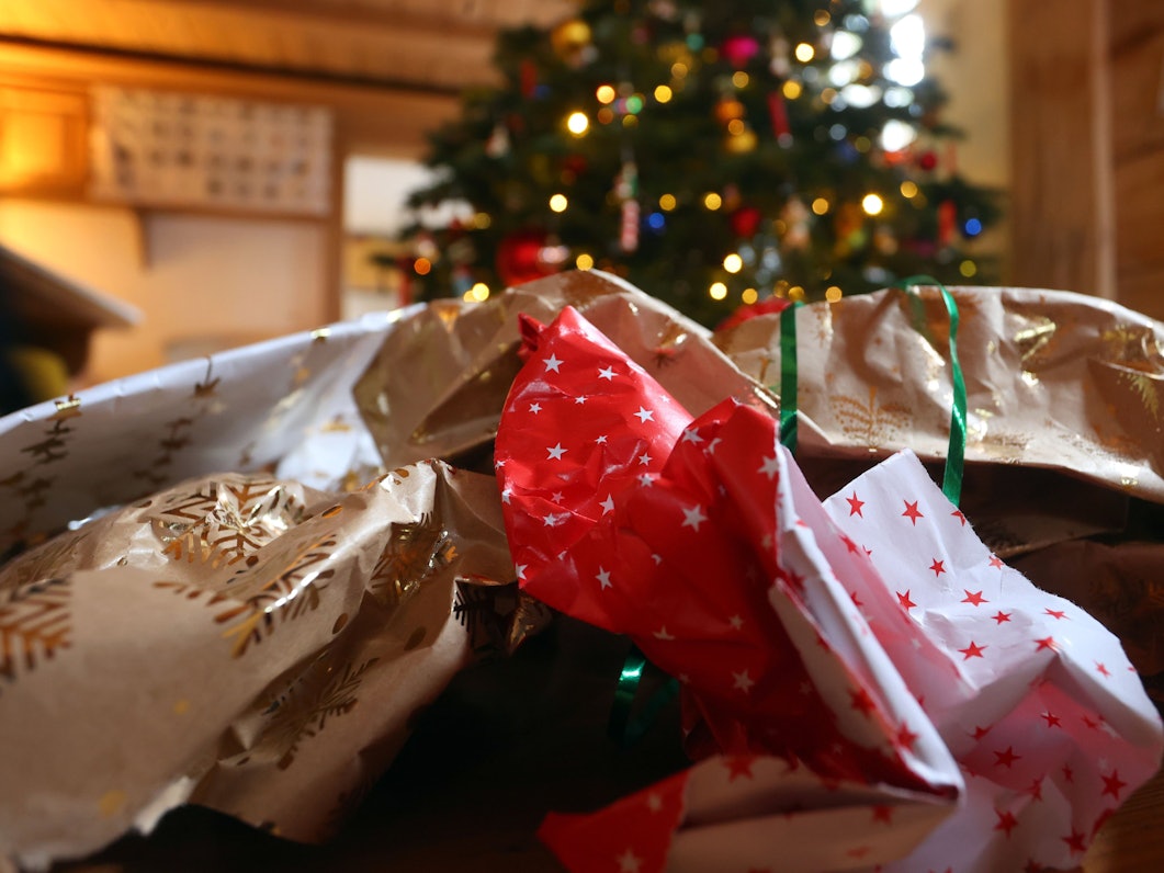 Geschenkpapier von ausgepackten Weihnachtsgeschenken liegt auf dem Boden eines Zimmers vor einem geschmücktem Weihnachtsbaum.