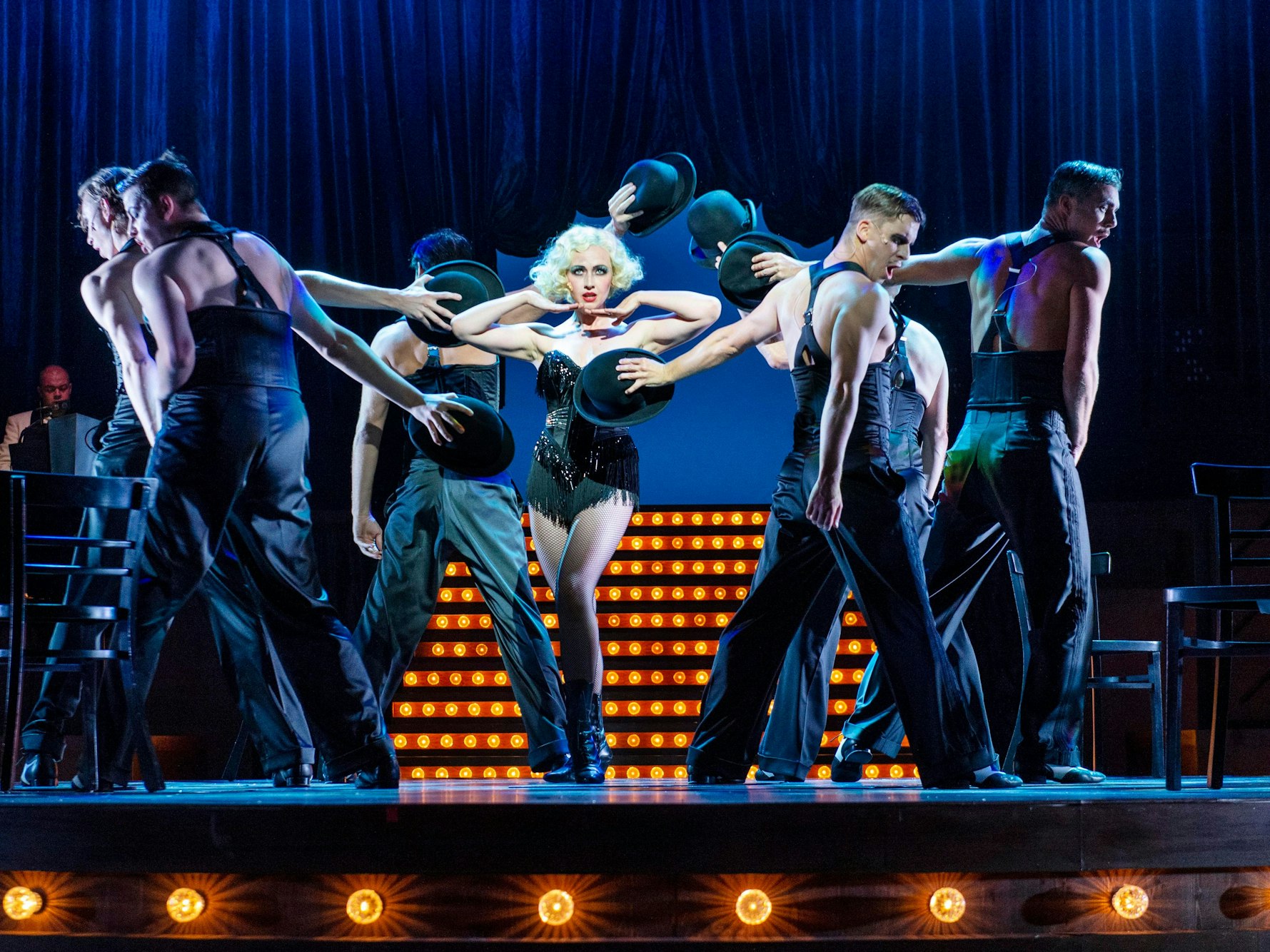 Darsteller und eine Darstellerin des Musicals „Chicago“ stehen in einer Tanzszene auf der Bühne.