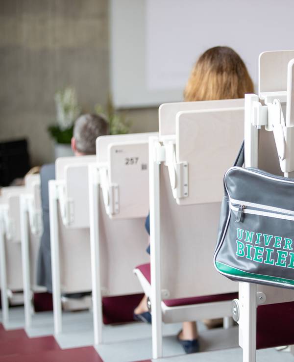 Eine Tasche mit der Aufschrift Universität Bielefeld hängt in einem Hörsaal.