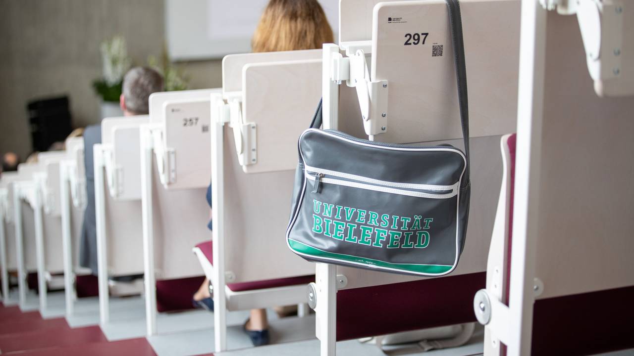 Eine Tasche mit der Aufschrift Universität Bielefeld hängt in einem Hörsaal.