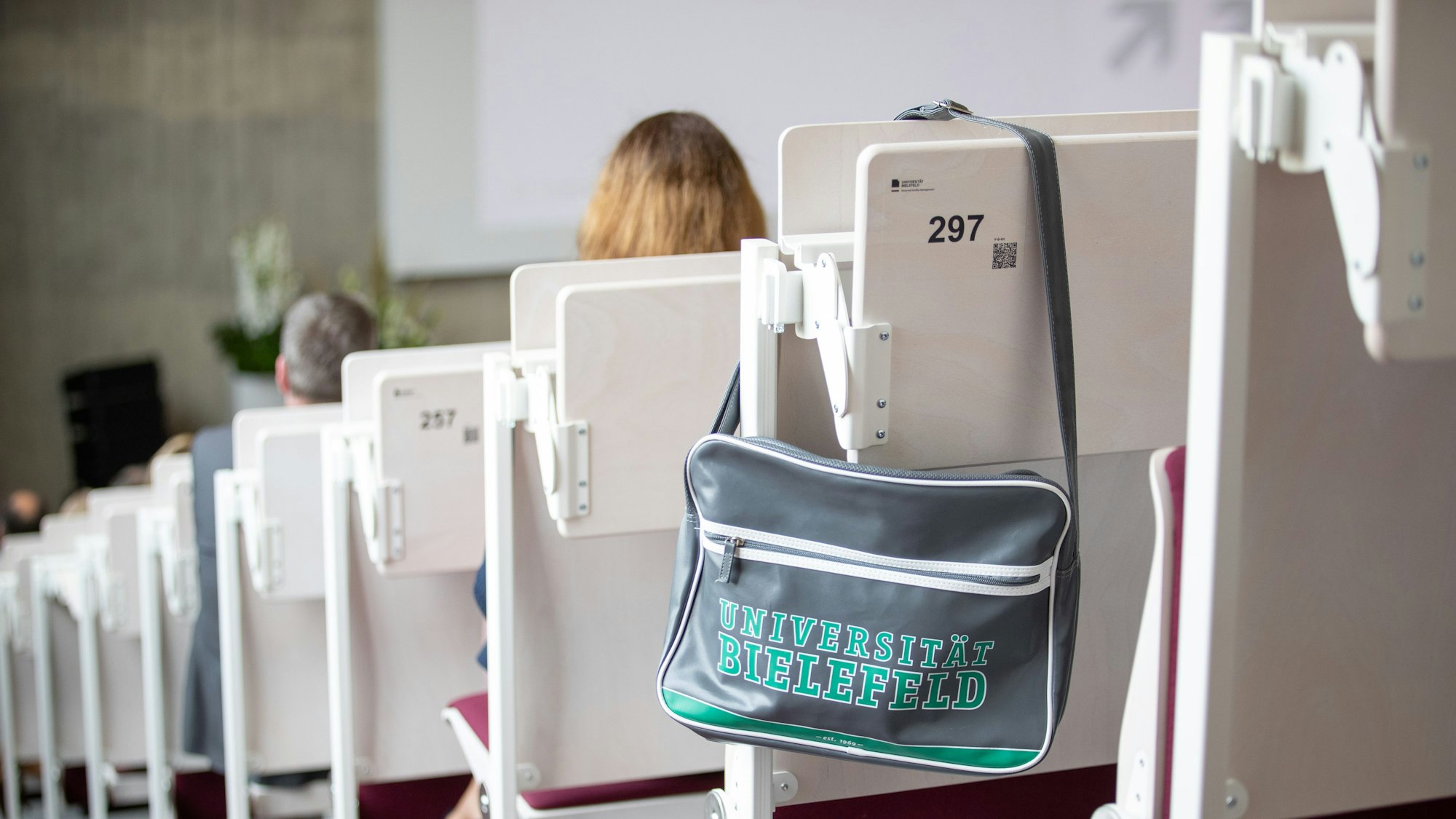 Eine Tasche mit der Aufschrift Universität Bielefeld hängt in einem Hörsaal.