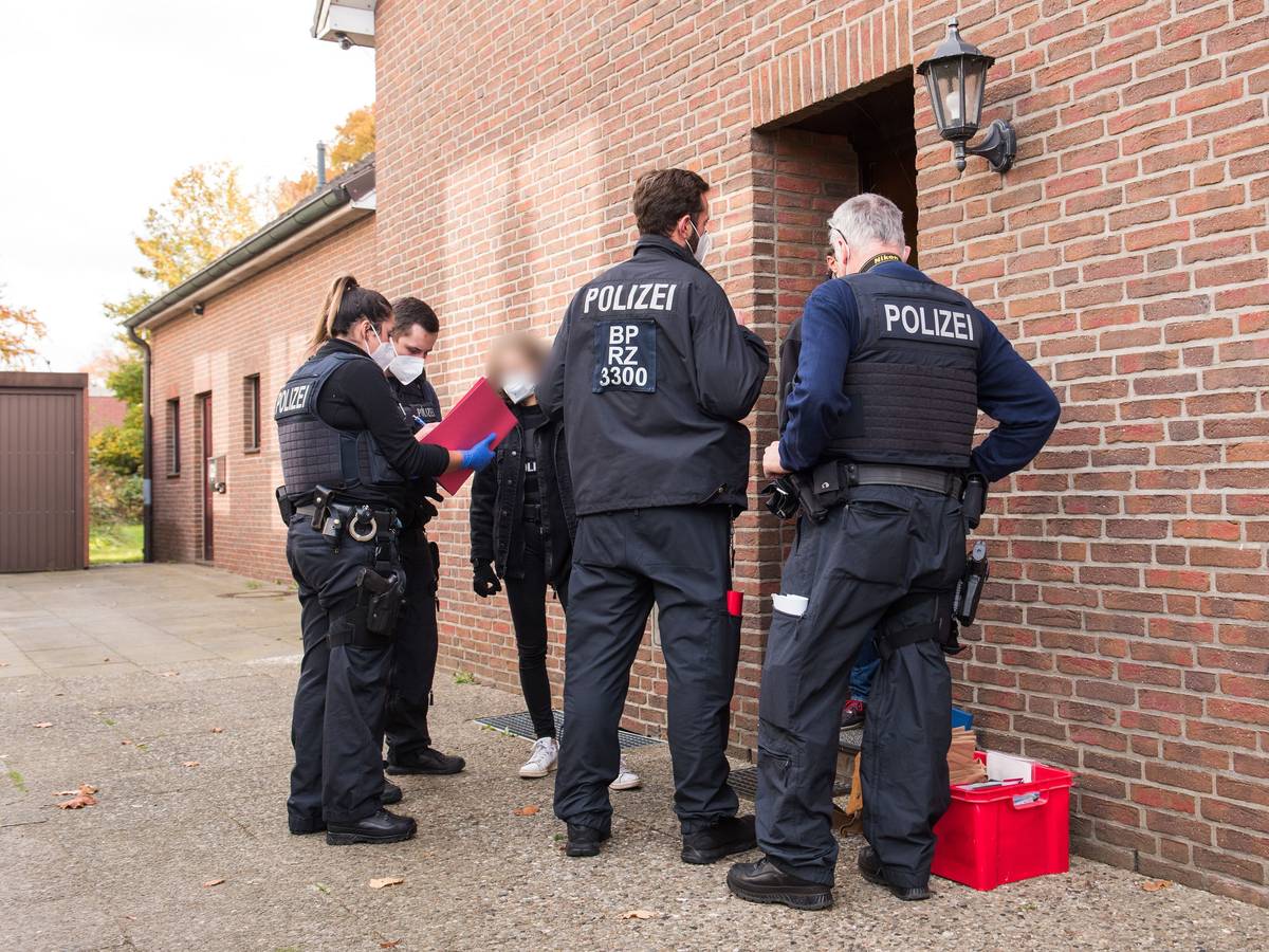 Einsatzkräfte der Bundespolizei stehen vor einem Wohnhaus und befragen eine Frau.