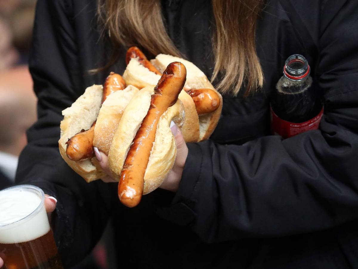 Eie Frau trägt mehrere Stadionwürstchen, Bier und eine Cola-Flasche zu ihrem Platz