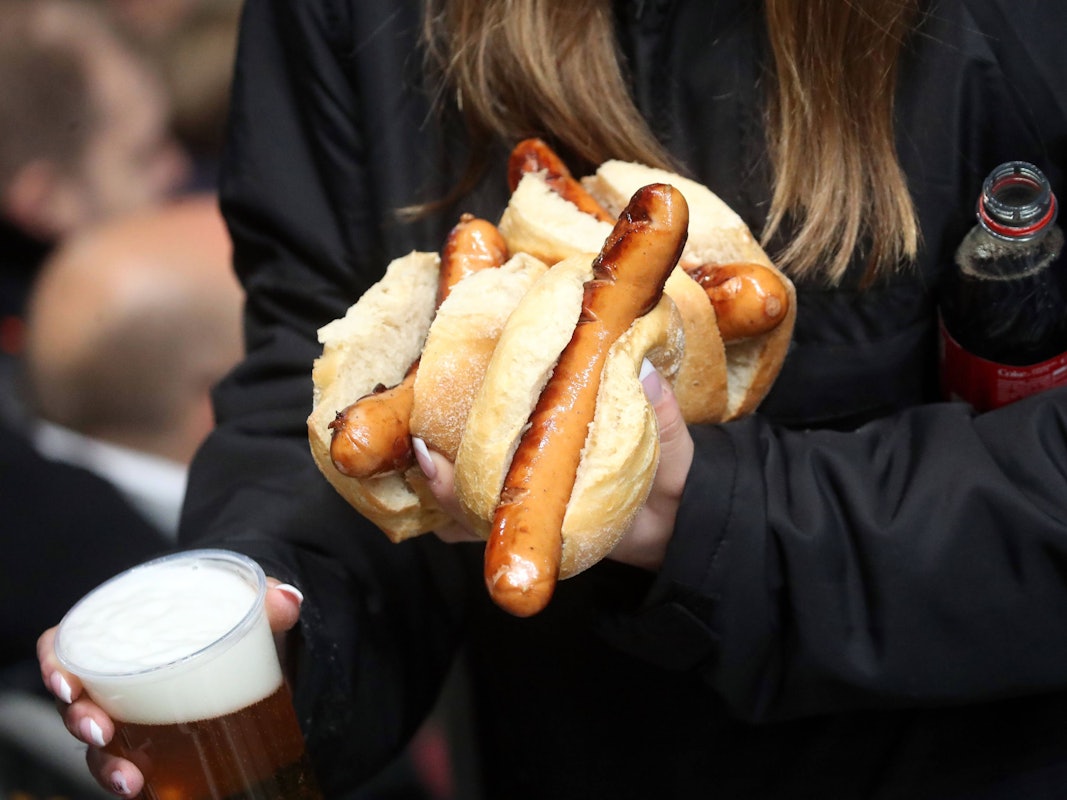 Eie Frau trägt mehrere Stadionwürstchen, Bier und eine Cola-Flasche zu ihrem Platz