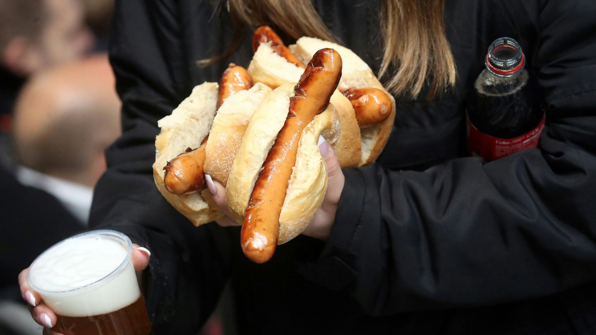 Eie Frau trägt mehrere Stadionwürstchen, Bier und eine Cola-Flasche zu ihrem Platz