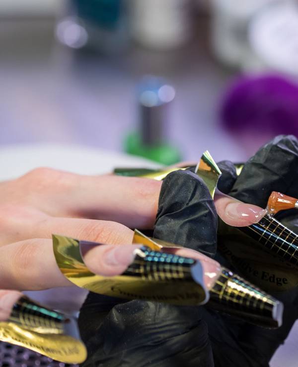 Eine Kosmetikerin trägt in einem Nagelstudio eine Gelschicht auf die Nägel einer Kundin auf.