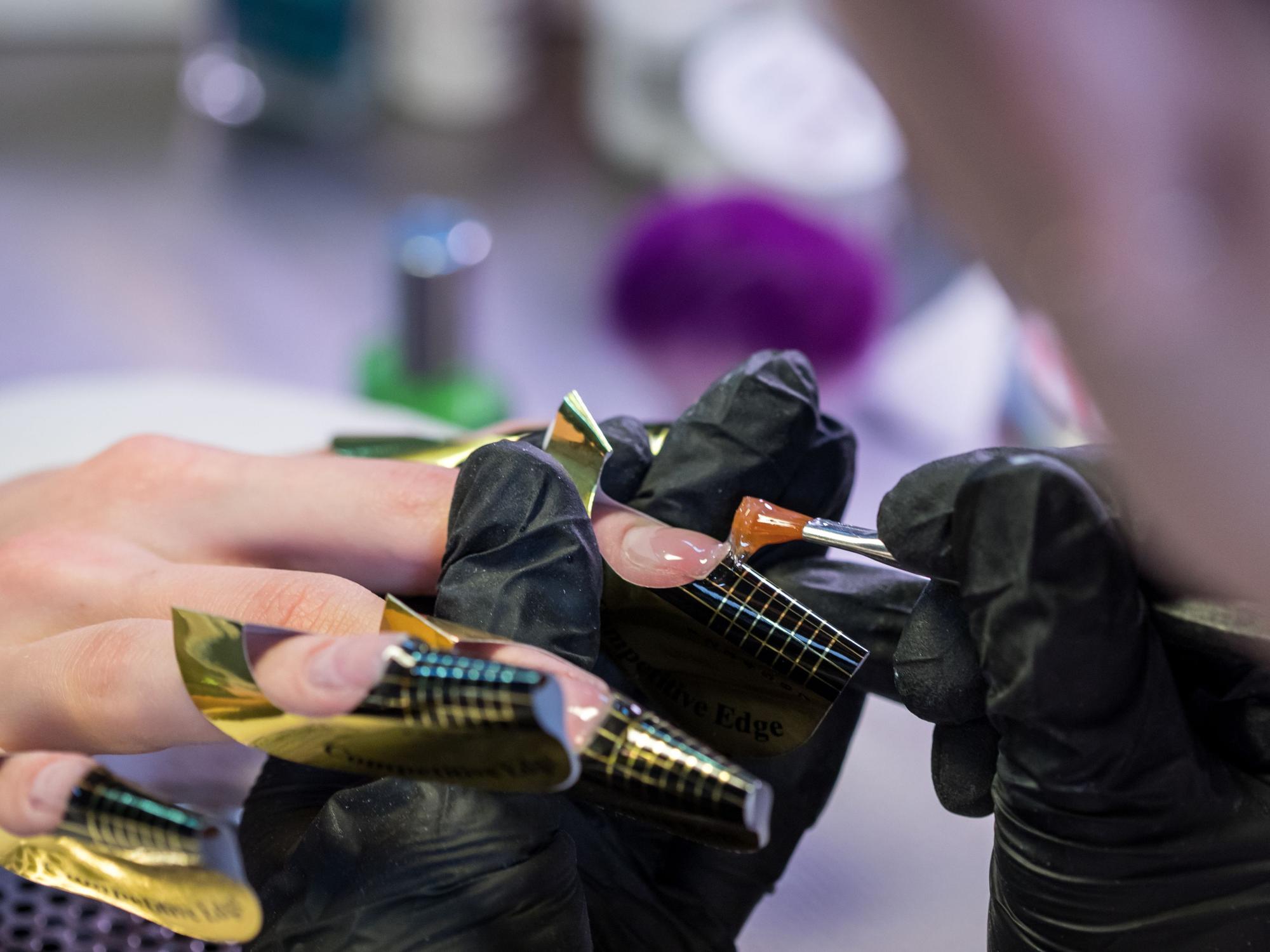 Eine Kosmetikerin trägt in einem Nagelstudio eine Gelschicht auf die Nägel einer Kundin auf.
