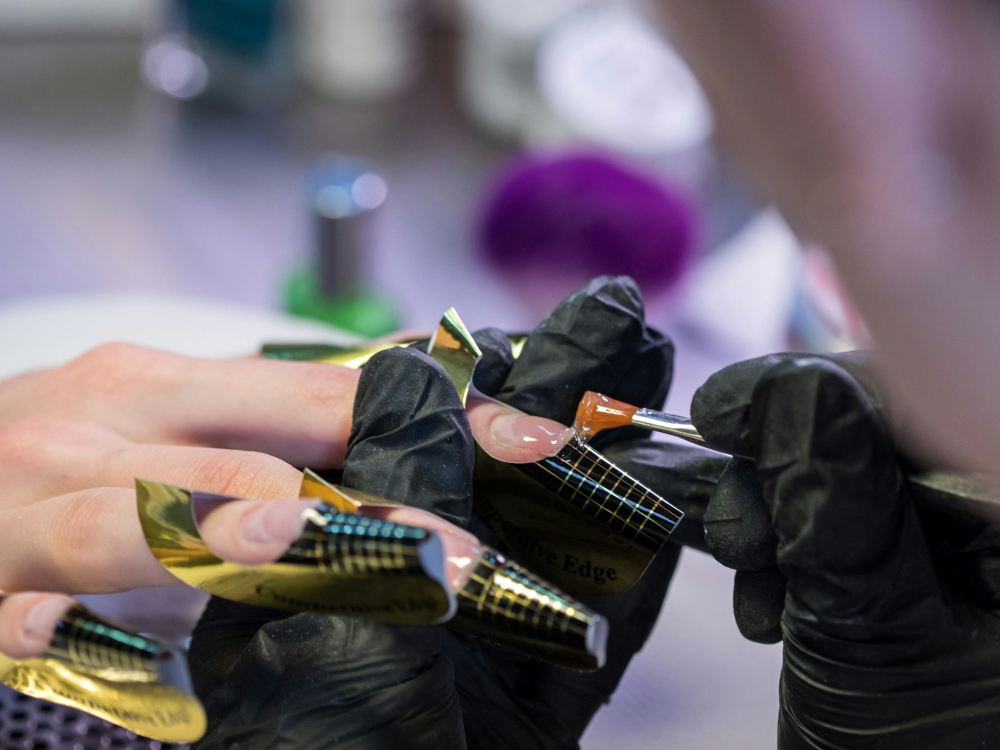 Eine Kosmetikerin trägt in einem Nagelstudio eine Gelschicht auf die Nägel einer Kundin auf.