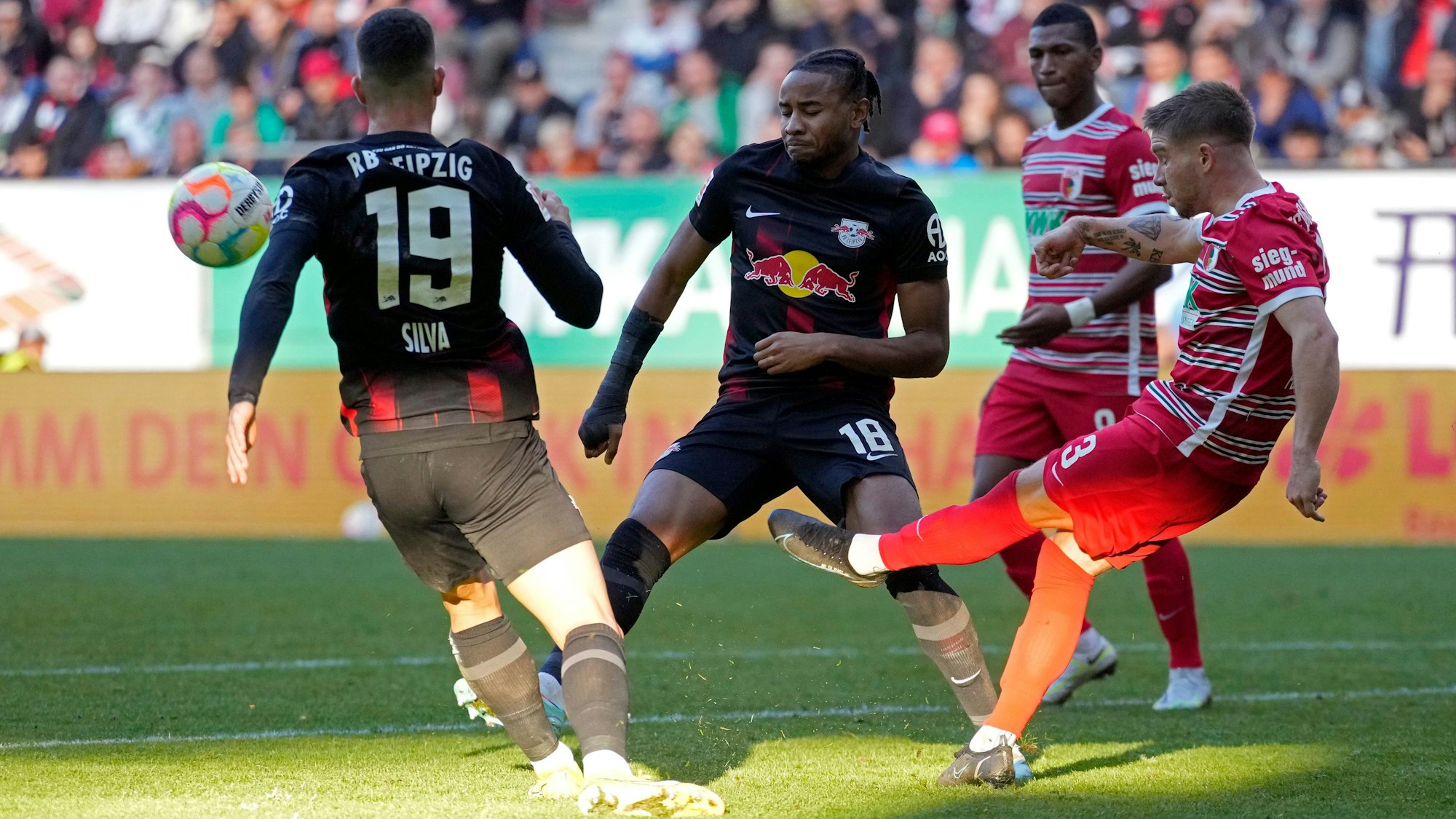 Die Leipziger Andre Silva und Christopher Nkunku versuchen Augsburg Mads Pedersen beim Schuss zu stören.
